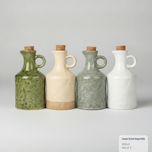 May include: Four ceramic oil and vinegar bottles with cork stoppers, each featuring a side handle and a 400ml capacity. The bottles are finished in green, cream, speckled grey, and white glazes, with a textured surface appearance.