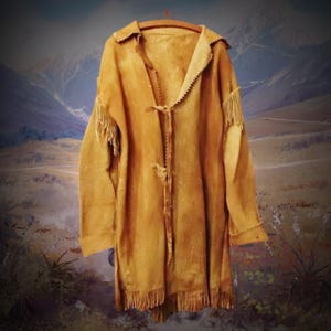 Könnte beinhalten: Eine lange, braune Lederjacke mit Fransen an den Ärmeln und am Saum. Die Jacke hat ein schlichtes Design mit einem Bindeverschluss vorne.