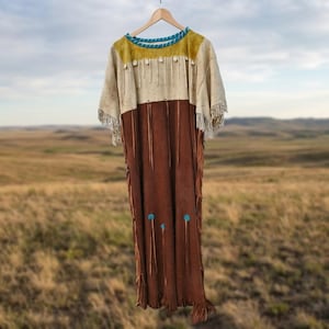 Könnte beinhalten: Ein Kleid aus Wildleder mit einem cremefarbenen Oberteil, einer senfgelben Passe und einem türkisfarbenen Halsausschnitt. Der untere Teil ist dunkelbraun mit langen Fransen, weißen Muschelakzenten und kleinen türkisfarbenen runden Verzierungen.