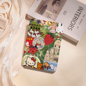 Puede incluir: Una funda rectangular cubierta de coloridas pegatinas con personajes de dibujos animados, fresas y texto japonés. La funda tiene un fondo verde y está decorada con varias imágenes, incluyendo Hello Kitty y un conejo.