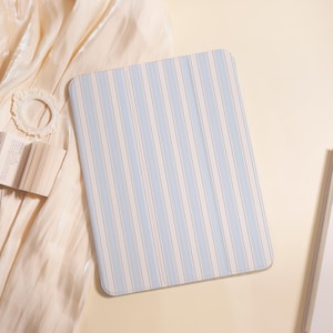 May include: A rectangular tablet case with a blue and white striped pattern. The stripes are vertical, with a dotted line running down the centre of each blue stripe. The case is on a cream-coloured surface.