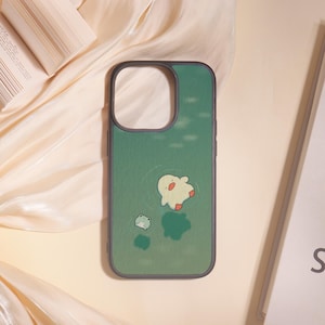 Pode incluir: Capa de telefone verde com um design de pato e sapo de desenho animado. A capa tem uma borda cinza escuro e um fundo verde com detalhes aquáticos. O pato é branco com detalhes vermelhos e o sapo é verde claro.