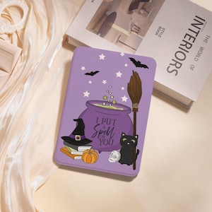 Könnte beinhalten: Eine lila Tablet-Hülle mit Halloween-Motiv. Die Hülle zeigt einen Kessel, einen Hexenhut, eine schwarze Katze, einen Besen, einen Kürbis, einen Totenkopf, Sterne und Fledermäuse. Der Text auf der Hülle lautet "I PUT A SPELL ON YOU."