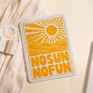 May include: Rectangular, yellow and white sign with the text "NO SUN NO FUN". The sign features a sun graphic with rays, and a mountain range. The sign is on a cream-colored surface.