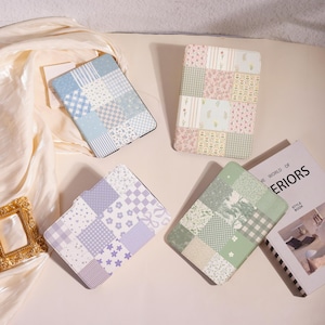 May include: Four tablet cases with patchwork designs in pastel colors. The cases feature patterns like gingham, floral, and stripes. One case is blue, another pink, a third purple, and the last green. A book with the title "THE WORLD OF INTERIORS" is also visible.