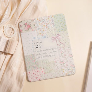 Pode incluir: Um livro com uma capa de design floral e patchwork, com rosas cor-de-rosa e pequenas flores. O texto "SALMO 37:5" e uma citação são visíveis. Um laço rosa adorna a capa. O livro está aberto.