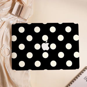 May include: A black laptop case featuring a white polka dot pattern. The Apple logo is visible in the center. The case is designed to fit a laptop and provides a stylish and protective cover.