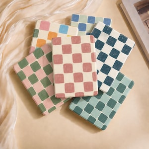 May include: A collection of five rectangular ceramic coasters, each featuring a distinct grid of colored squares. The patterns include combinations of pink, green, blue, orange, and cream, arranged in a checkerboard layout on each individual piece.