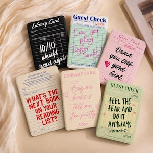 Pode incluir: Seis cadernos retangulares com designs de fichas de biblioteca e notas de restaurante vintage. As capas exibem várias frases impressas, incluindo "10/10 would read again," "Can you play Taylor Swift," "Damn you look good Girl," "WHAT'S THE NEXT BOOK ON YOUR READING LIST?," "Buy me books & Tell me I'm pretty," e "FEEL THE FEAR AND DO IT ANYWAYS."