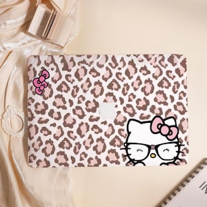 May include: A laptop case featuring a pink and brown leopard print design. The case has a cartoon image of a white cat with glasses and a pink bow. A pink bow sticker is also on the case. The Apple logo is visible.