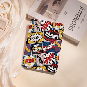 May include: A comic book-themed notebook with a colorful pattern of action words like "BOOM!" and "ZAAAP!" in speech bubbles. The design features bold colors, including red, yellow, blue, and black, creating a dynamic and eye-catching aesthetic. The notebook is rectangular.