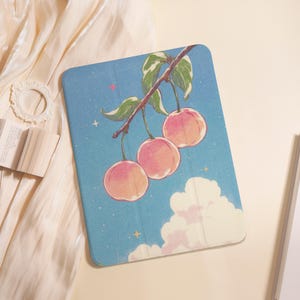 May include: A rectangular tablet case featuring a blue sky background with white clouds, small yellow stars, and a branch with three pink peaches hanging from it. The design includes green leaves on the branch and a subtle textured finish overall.