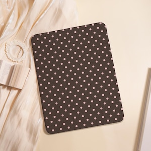Peut inclure: Un tapis rectangulaire marron avec un motif répété de petits pois roses espacés uniformément. Le tapis est posé sur une surface crème, avec un livre et un cadre décoratif en arrière-plan.