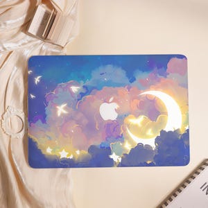 May include: A laptop skin featuring a dreamy night sky design. The artwork includes a glowing crescent moon, fluffy clouds in shades of blue, purple, and yellow, and a white Apple logo. Small white birds and stars are scattered across the sky.