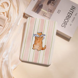 May include: A rectangular case featuring a ginger cat illustration holding two fish. The case has a striped pattern in pink, green, and white. The image is set against a white background.