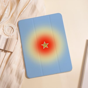 May include: A light blue tablet case featuring a central gradient design that transitions from a vibrant red center to a soft yellow halo. A single, five-pointed gold star is positioned directly in the middle of the red circular gradient.