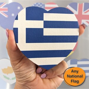 Peut inclure: Un objet en forme de cœur avec le drapeau grec, tenu dans une main. Le drapeau a des rayures bleues et blanches et une croix blanche. D'autres objets en forme de cœur avec des drapeaux nationaux sont en arrière-plan. Le texte sur l'image dit "Any National Flag."