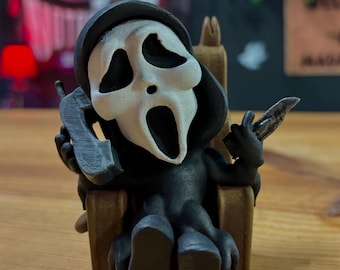 May include: A black and white figurine of the Ghostface killer from the Scream movie franchise. The figure is seated in a wooden chair, holding a knife and a phone. The figure has a white mask with black eye holes and a gaping mouth.