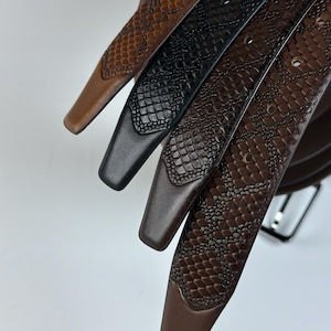 May include: Close-up of four leather belts in shades of brown and black. The belts have a textured, snakeskin-like pattern. The tips of the belts are a solid color, and the buckles are visible in the background. The belts are likely for fashion or everyday wear.