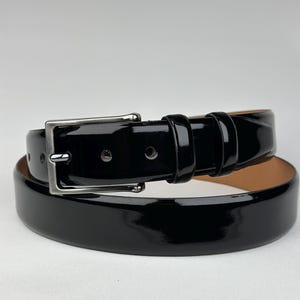 Pode incluir: Um cinto de couro preto com uma fivela de prata. O cinto &eacute; brilhante e tem um acabamento polido.