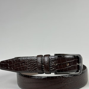 Peut inclure: Une ceinture marron fonc&eacute; avec un motif textur&eacute; en forme de crocodile. La ceinture est dot&eacute;e d'une boucle rectangulaire de couleur argent&eacute;e et d'une boucle de ceinture assortie. La ceinture en cuir est con&ccedil;ue pour un usage quotidien.