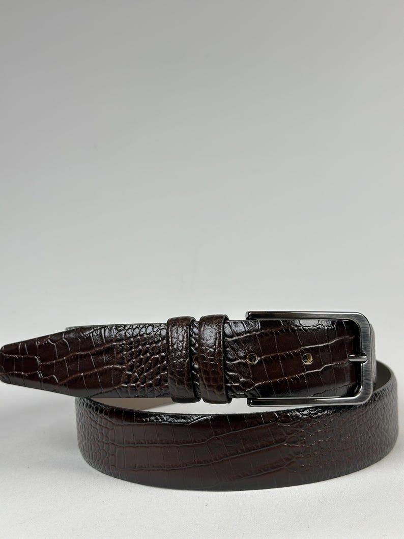 Peut inclure: Une ceinture marron fonc&eacute; avec un motif textur&eacute; en forme de crocodile. La ceinture est dot&eacute;e d'une boucle rectangulaire de couleur argent&eacute;e et d'une boucle de ceinture assortie. La ceinture en cuir est con&ccedil;ue pour un usage quotidien.
