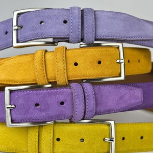 May include: Four suede belts in a stack, two yellow and two purple. The belts have silver buckles.