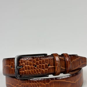 Peut inclure: Une ceinture en cuir marron avec un motif textur&eacute; en forme de crocodile. La boucle rectangulaire et le passant sont de couleur canon de fusil. Un accessoire classique.