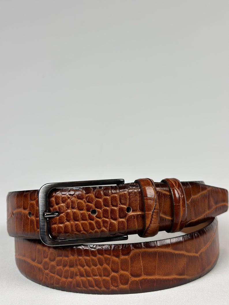 Peut inclure: Une ceinture en cuir marron avec un motif textur&eacute; en forme de crocodile. La boucle rectangulaire et le passant sont de couleur canon de fusil. Un accessoire classique.