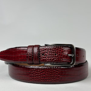 Peut inclure: Une ceinture en cuir bordeaux avec un motif textur&eacute; en forme de crocodile. La ceinture est dot&eacute;e d'une boucle rectangulaire de couleur argent&eacute;e et de trous d'ajustement. La ceinture est con&ccedil;ue pour les pantalons. Mesure environ 100 cm.