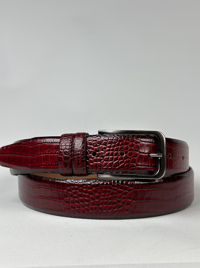 Peut inclure: Une ceinture en cuir bordeaux avec un motif textur&eacute; en forme de crocodile. La ceinture est dot&eacute;e d'une boucle rectangulaire de couleur argent&eacute;e et de trous d'ajustement. La ceinture est con&ccedil;ue pour les pantalons. Mesure environ 100 cm.