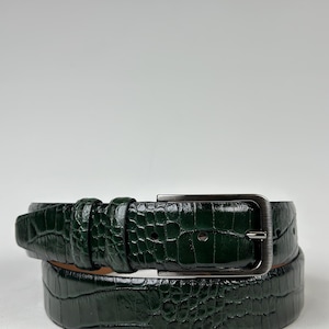 Peut inclure: Une ceinture vert fonc&eacute; avec un motif textur&eacute; en forme de crocodile. La ceinture est dot&eacute;e d'une boucle rectangulaire de couleur argent&eacute;e et d'une boucle assortie. La ceinture en cuir est enroul&eacute;e, montrant la texture et la couleur.