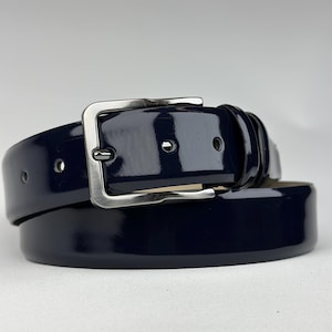 Pode incluir: Um cinto de couro azul escuro com uma fivela prateada. O cinto &eacute; brilhante e tem um acabamento liso.
