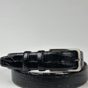 Peut inclure: Une ceinture noire avec un motif textur&eacute; en forme de crocodile. La ceinture est dot&eacute;e d'une boucle rectangulaire argent&eacute;e et de deux passants assortis. La ceinture en cuir est enroul&eacute;e.
