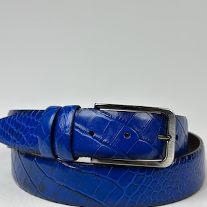 Peut inclure: Une ceinture bleu vif enroul&eacute;e, avec un motif textur&eacute; en forme de peau de crocodile. La ceinture est dot&eacute;e d'une boucle rectangulaire de couleur argent&eacute;e. Cette ceinture en cuir est un accessoire &eacute;l&eacute;gant.