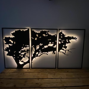 May include: A three-piece wall art set featuring a black silhouette of a tree with branches extending across all three panels. The panels are illuminated from behind, creating a glowing effect.