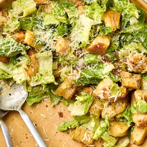 Puede incluir: Primer plano de un bol de ensalada César con lechuga romana, picatostes, queso parmesano rallado y un aderezo cremoso.