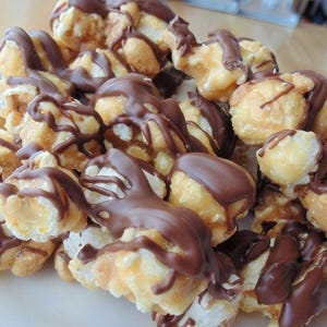 Puede incluir: Primer plano de palomitas de maíz rociadas con chocolate derretido. Las palomitas de maíz son de color marrón claro y el chocolate es de color marrón oscuro.