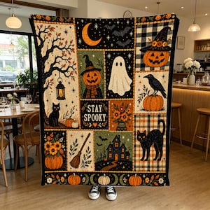 Könnte beinhalten: Eine rechteckige Wohndecke mit Patchwork-Design und Halloween-Motiven wie Kürbissen, einem Geist, einer schwarzen Katze, einer Krähe, einem Spukhaus, einem Besen und einer Mondsichel. Der Text STAY SPOOKY ist in der Mitte abgebildet.