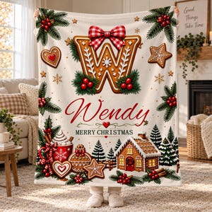 May include: A cream-colored fleece blanket featuring a large gingerbread letter W topped with a red and white checkered bow, the name Wendy, and the text Merry Christmas. The design includes gingerbread cookies, holly, and a gingerbread house.