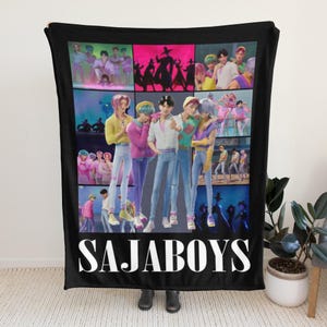 May include: Black blanket featuring a collage of images with a group of people in various poses. The blanket has the word "SAJABOYS" in large white letters at the bottom. The images are in a grid pattern.