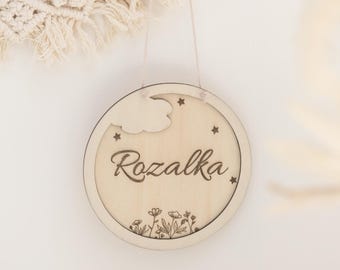 Peut inclure: Une pancarte ronde en bois avec un nuage découpé et des étoiles, le nom "Rozalka" est gravé en écriture cursive, et il y a de petits motifs floraux en bas.