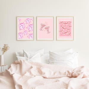 May include: Three framed prints with pink backgrounds. The left print features a pink disco ball pattern. The centre print features two pink champagne glasses. The right print features a pink bow pattern and the text "All I Need Is More Pink".