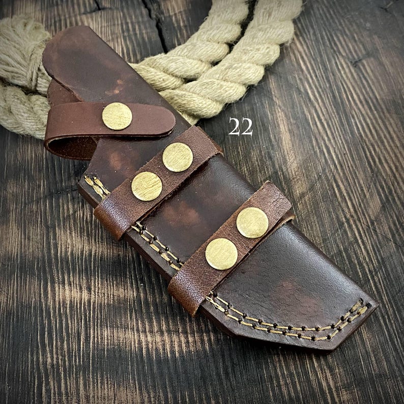 May include: A brown leather knife sheath with a stitched design and brass rivets. The sheath has a belt loop and is designed to hold a knife securely.