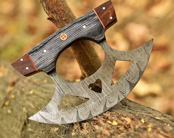 May include: A Damascus steel knife with a wooden handle and a unique design. The blade has a heart-shaped hole and two other holes. The handle is made of dark wood with a red stripe. The knife is resting on a piece of wood. X-1060