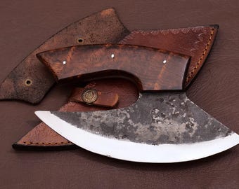 May include: A handmade, curved,  black and silver knife with a wooden handle. The knife is in a brown leather sheath.