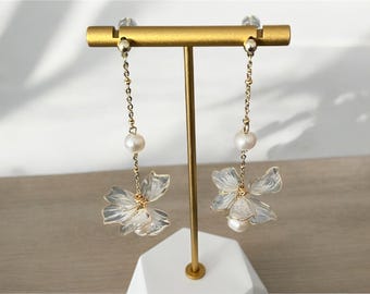 May include: A pair of gold dangle earrings with a white pearl and a clear flower charm.
