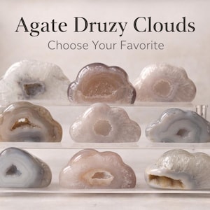 May include: Nine agate druzy cloud formations in various colors, including white, brown, and gray, are displayed on a clear acrylic stand. The text "Agate Druzy Clouds" and "Choose Your Favorite" are at the top of the image.