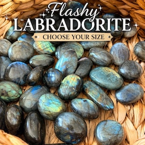 May include: A collection of polished labradorite stones in various shapes and sizes, with iridescent blue, green, and gold flashes. The stones are displayed in a woven basket. Text on the image reads "Flashy Labradorite, Choose Your Size."