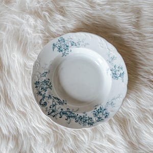 May include: White ceramic plate with a scalloped edge and a teal floral design. The plate features a central well and is decorated with detailed botanical patterns around the rim. A vintage-style serving dish.